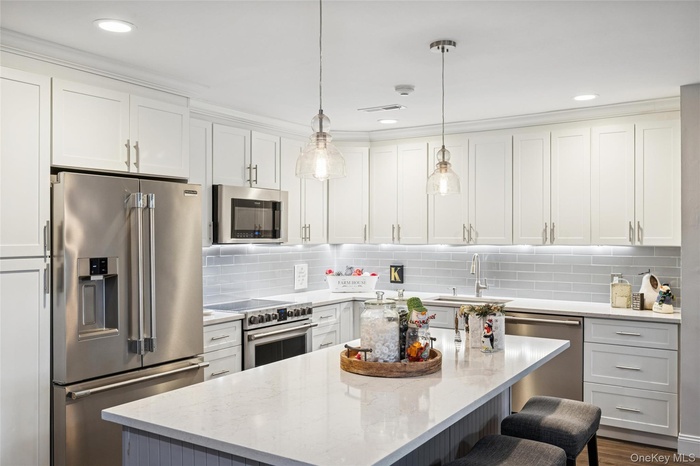Kitchen featuring stainless steel appliances, white cabinetry, a center island, hanging light fixtures, and recessed lighting