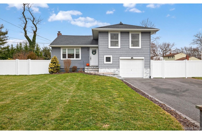 Tri-level home with driveway, an attached garage, a chimney, and a shingled roof