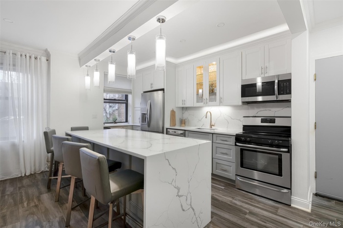 Kitchen featuring stainless steel appliances, crown molding, pendant lighting, a kitchen breakfast bar, and light stone countertops