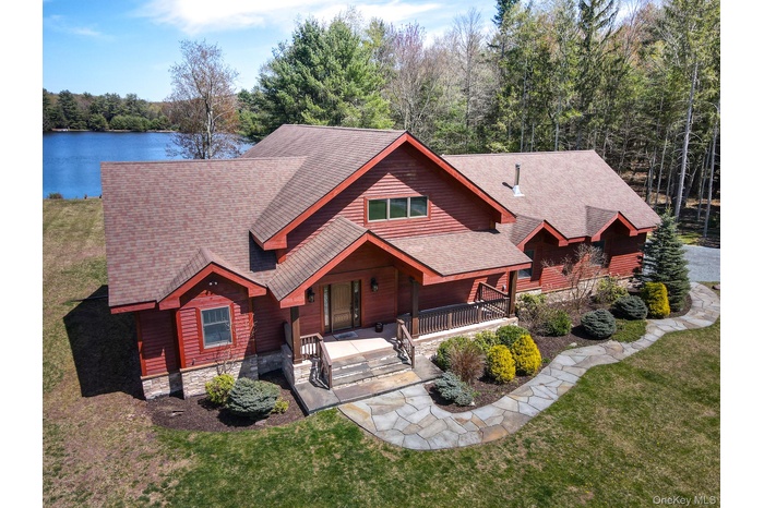 View of front of home with a porch, roof with shingles, stone siding, and a front lawn