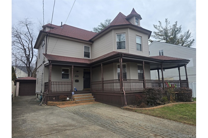 Victorian home featuring covered porch, an outdoor structure, roof with shingles, and a garage