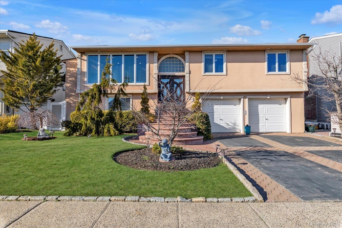 Raised ranch featuring a chimney, stucco siding, a front lawn, a garage, and aphalt driveway