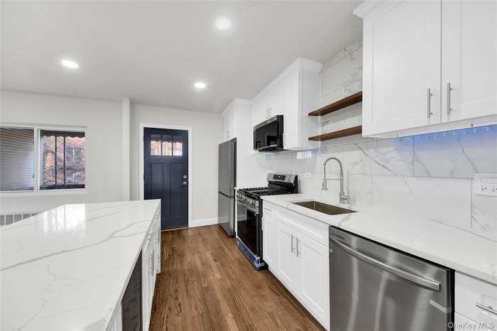 Kitchen featuring open shelves, white cabinets, appliances with stainless steel finishes, light stone countertops, and recessed lighting