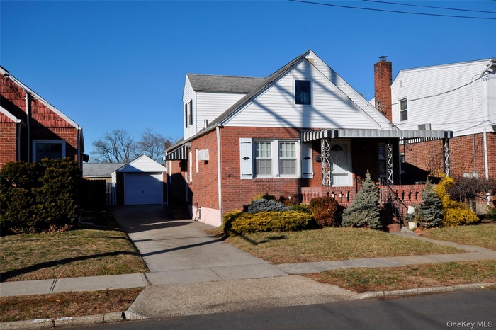 Bungalow-style home featuring an outdoor structure, a front lawn, brick siding, concrete driveway, and a porch