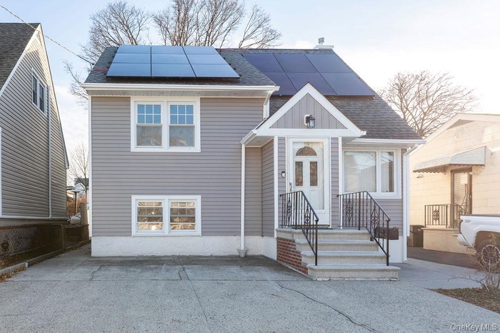 View of front facade featuring a shingled roof and roof mounted solar panels