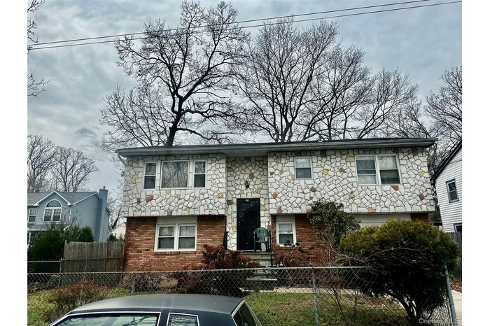 Bi-level home featuring a fenced front yard, stone siding, and brick siding