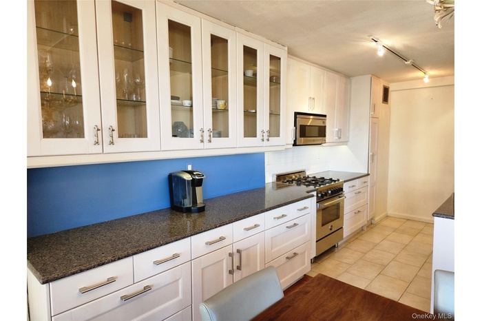 Kitchen with light tile patterned floors, dark stone counters, white cabinets, appliances with stainless steel finishes, and tasteful backsplash
