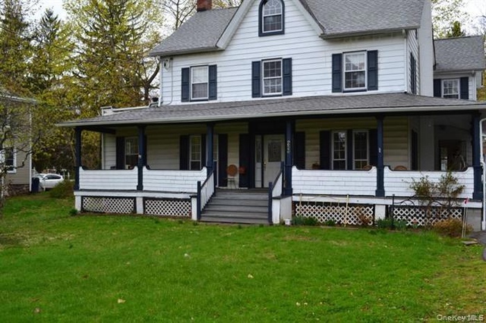 Country-style home with a chimney, a porch, a front lawn, and roof with shingles