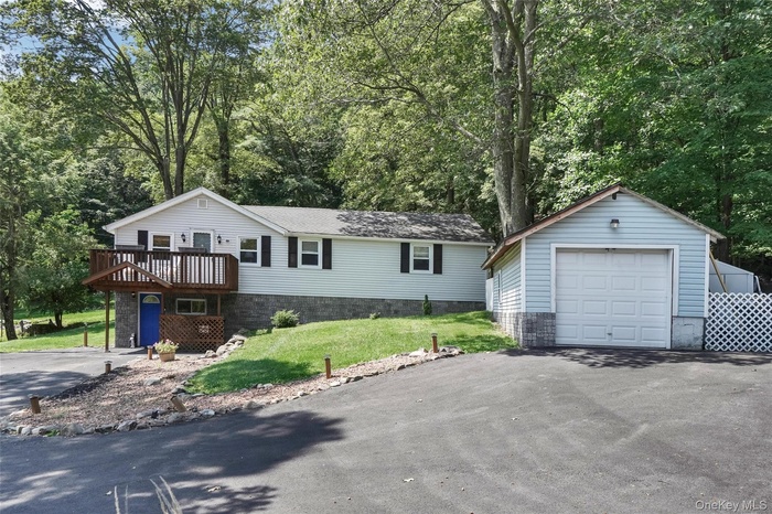 View of front of house featuring an outdoor structure, a front lawn, a detached garage, driveway, and view of wooded area