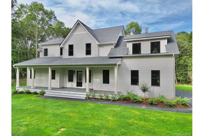 Modern farmhouse with a shingled roof, board and batten siding, a porch, and a front lawn