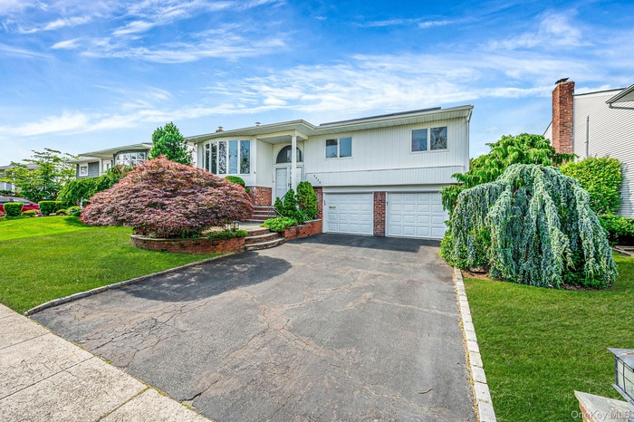 Split foyer home featuring asphalt driveway, brick siding, a garage, and a front yard