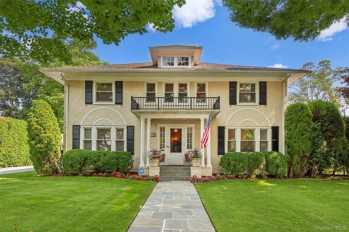 Colonial-style house with a front yard, stucco siding, and a balcony