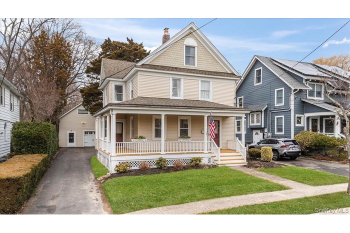 Victorian house featuring a porch, a chimney, a front yard, roof with shingles, and driveway