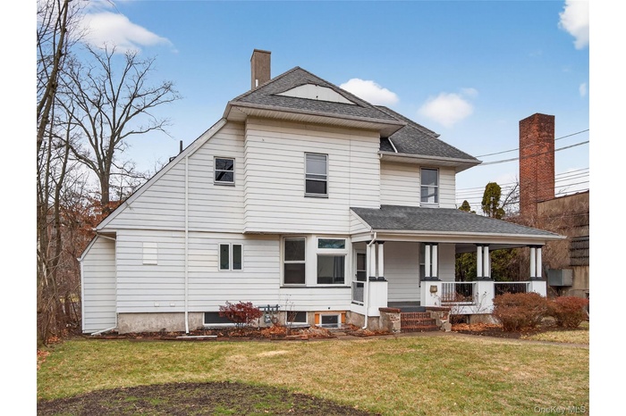 Rear view of house with a porch, a lawn, a shingled roof, and a chimney