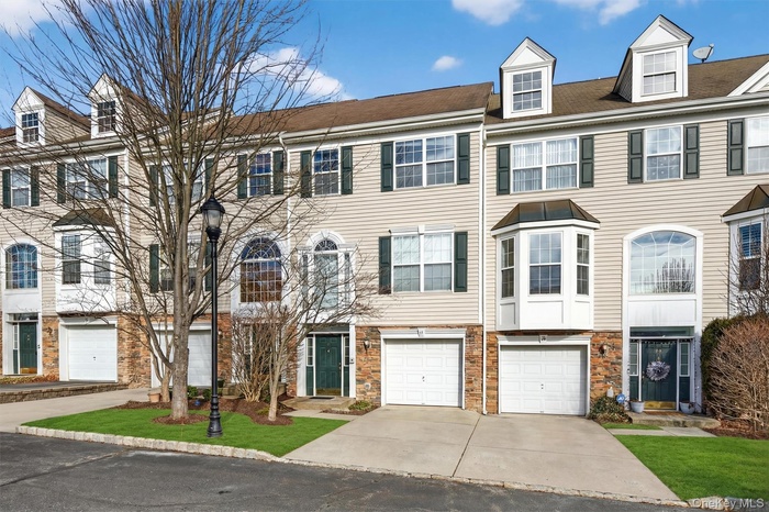 Colonial house featuring driveway, a garage, and stone siding