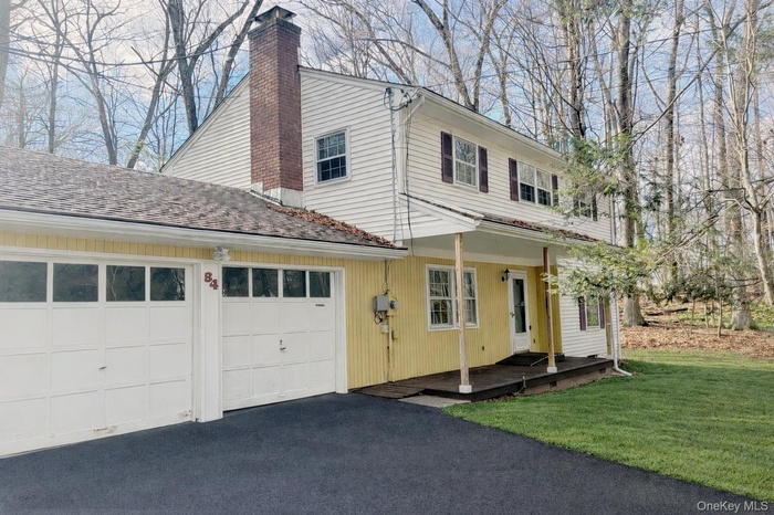 View of front of property with a chimney, asphalt driveway, a garage, and a front lawn