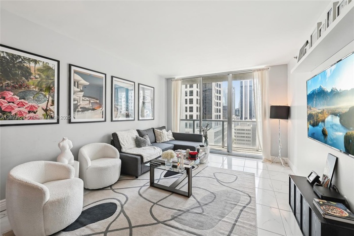 Modern open-concept living room with floor-to-ceiling windows offering panoramic views of Brickell skyline and Miami River. Luxury high-rise condo in 