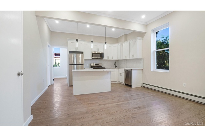 Kitchen featuring a center island, decorative light fixtures, tasteful backsplash, white cabinetry, and light wood-style flooring