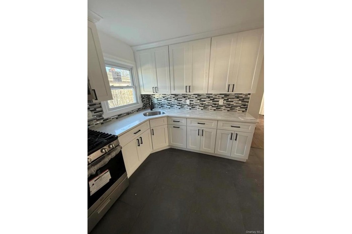 Kitchen featuring stainless steel gas range oven, a sink, backsplash, light countertops, and white cabinets