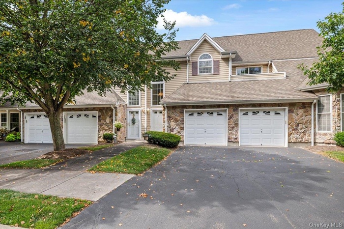 Traditional home featuring stone siding, driveway, an attached garage, and roof with shingles