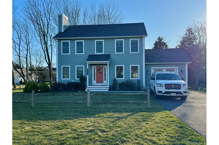 View of front of house featuring roof with shingles, a chimney, asphalt driveway, a garage, and a front lawn