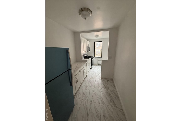 Kitchen with stainless steel appliances, white cabinets, light marble finish floors, light stone countertops, microwave