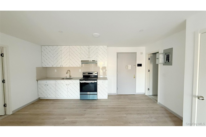 Kitchen featuring stainless steel electric range oven, tasteful backsplash, light wood-style floors, white cabinetry, and electric panel