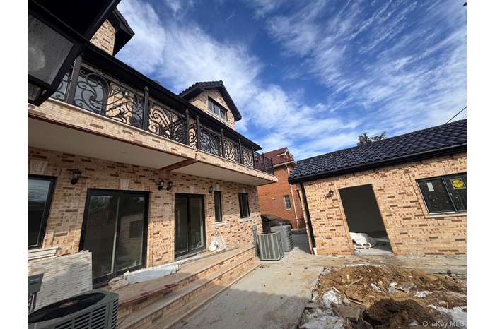 Back of house with a tiled roof, cooling unit, brick siding, and a balcony