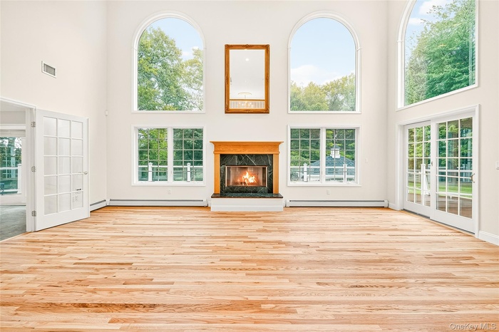 living room featuring a high ceiling, a fireplace, light wood-type flooring, and baseboard heating