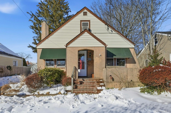Tudor style Cape Cod front of home featuring awnings and chimney
