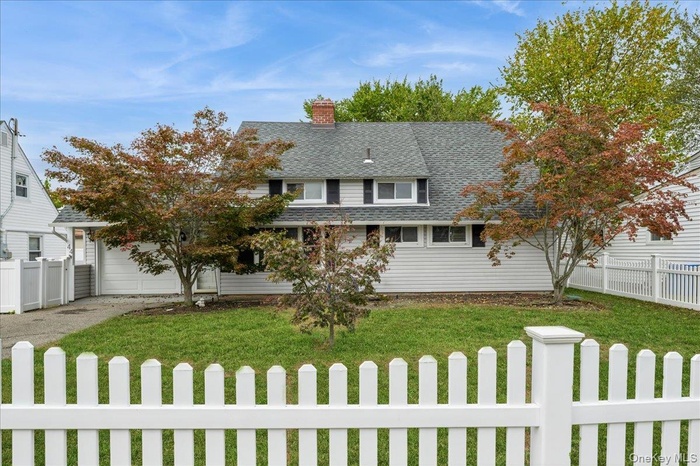 View of front of house featuring a fenced front yard, a shingled roof, a chimney, and driveway