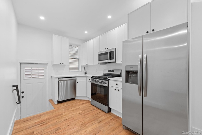 Kitchen featuring appliances with stainless steel finishes, light countertops, white cabinets, light wood-style flooring, and recessed lighting