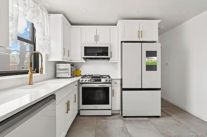 Kitchen with white cabinetry, stainless steel appliances, light stone countertops, and tasteful backsplash