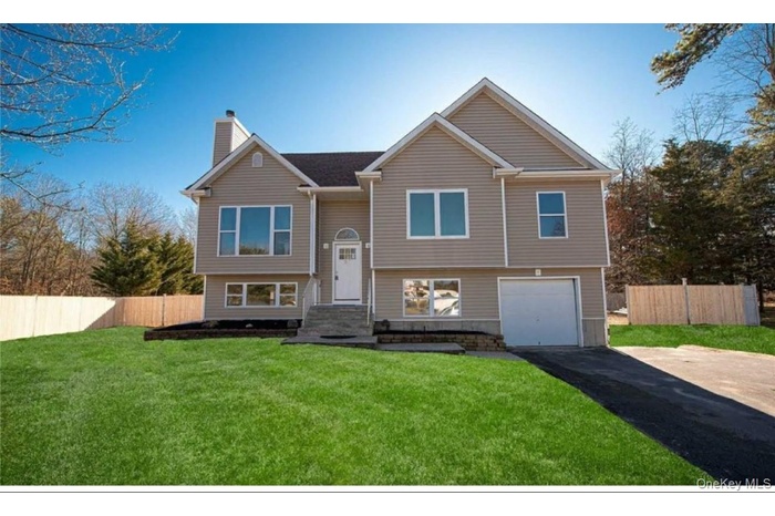 Bi-level home with asphalt driveway, an attached garage, a chimney, and stone siding