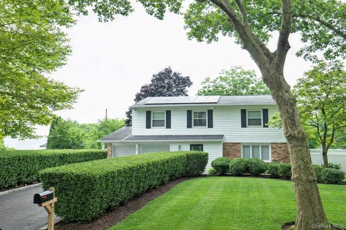 View of front of house featuring brick siding, solar panels & shrubs
