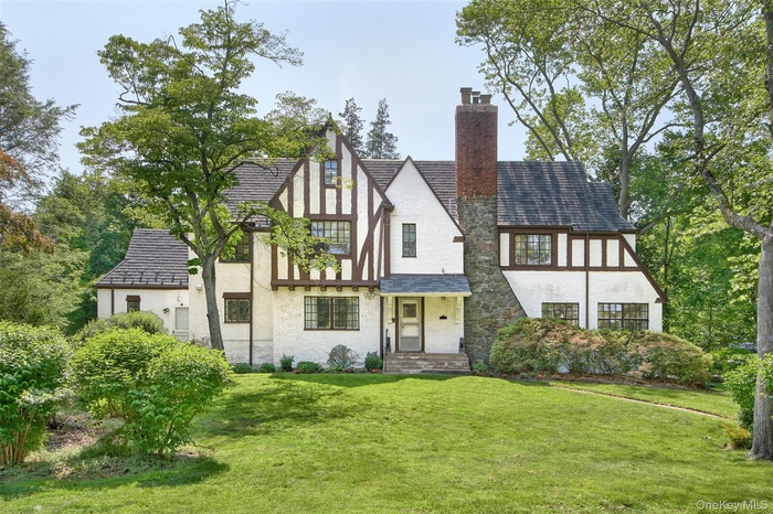 Tudor house with stucco siding, a chimney, a front lawn, and stone siding