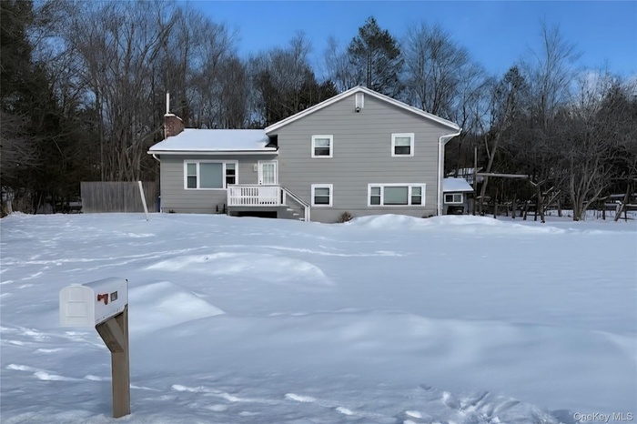 Snow covered rear of property with a chimney and view of scattered trees