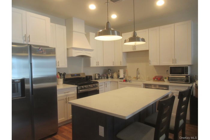 Kitchen featuring stainless steel appliances, pendant lighting, a kitchen island, and white cabinetry