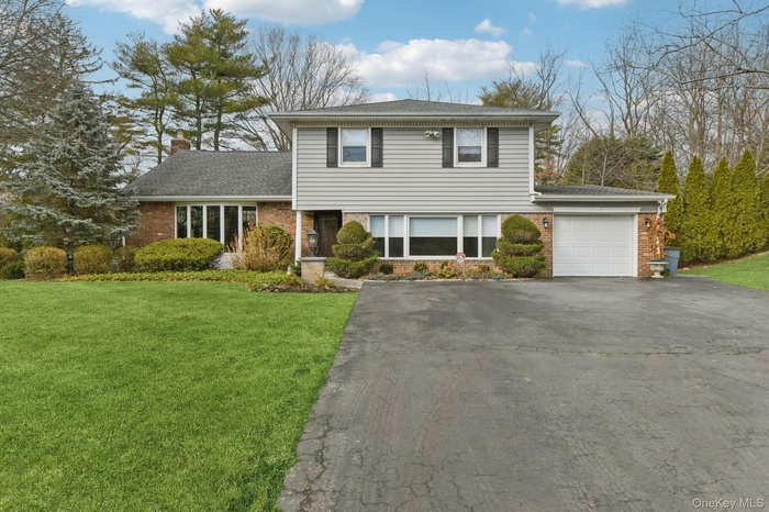 Split level home with a front yard, driveway, brick siding, and an attached garage