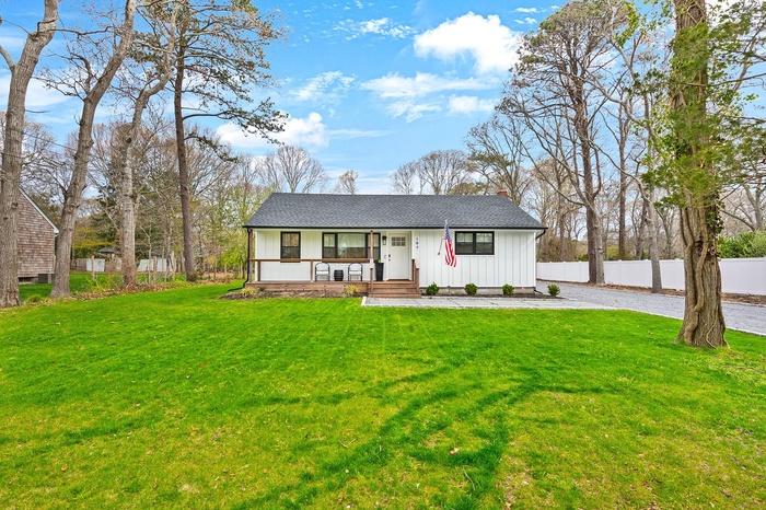 View of front of house with board and batten siding, covered porch, driveway, and a chimney