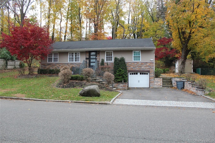 Ranch-style home featuring stone siding, driveway, a front yard, and a garage