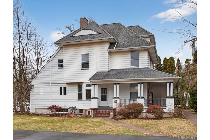 View of front of home featuring a porch, a chimney, a front lawn, and roof with shingles