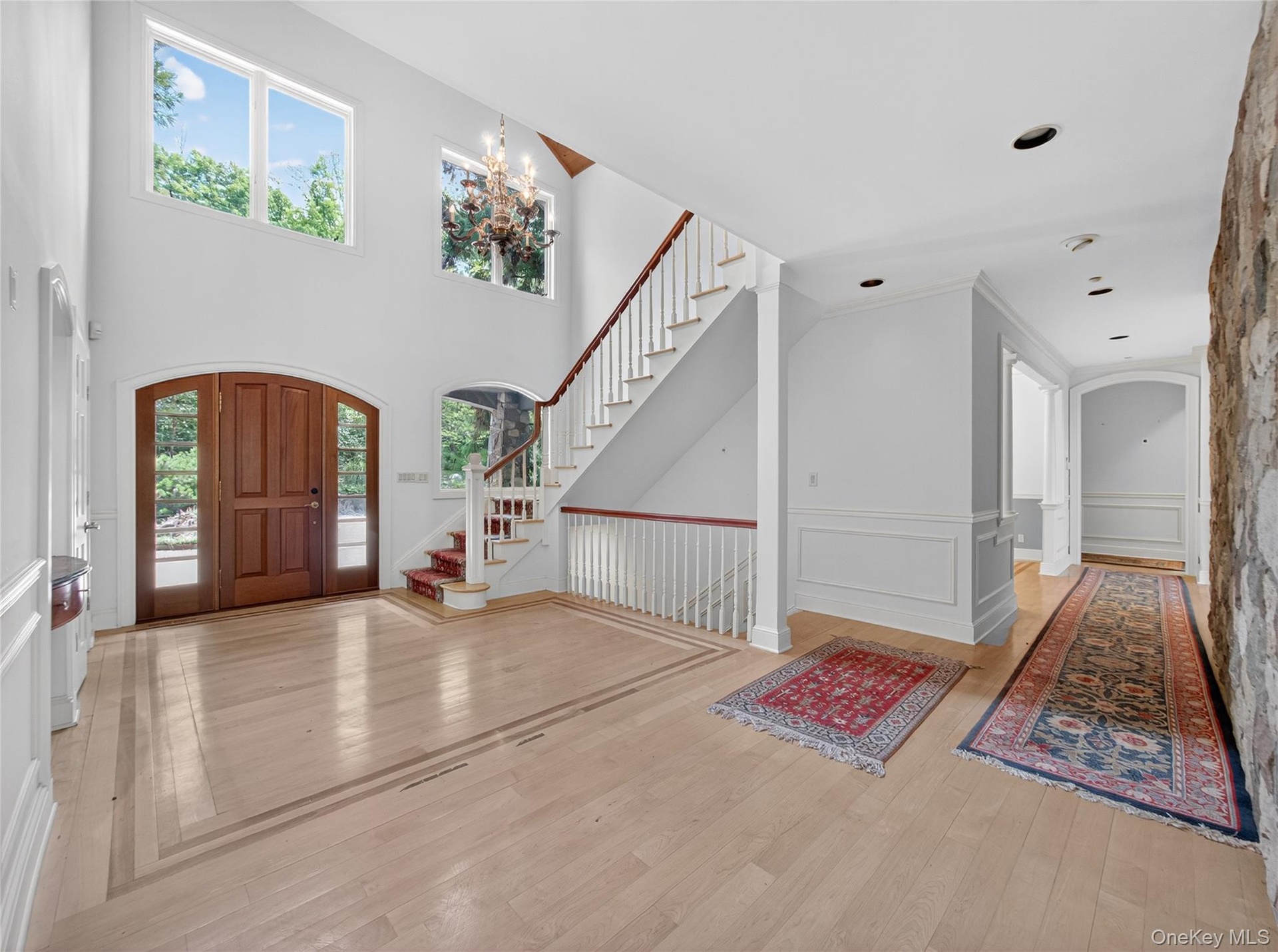 Entryway with arched walkways, stairs, light wood-style flooring, a wainscoted wall, and a decorative wall