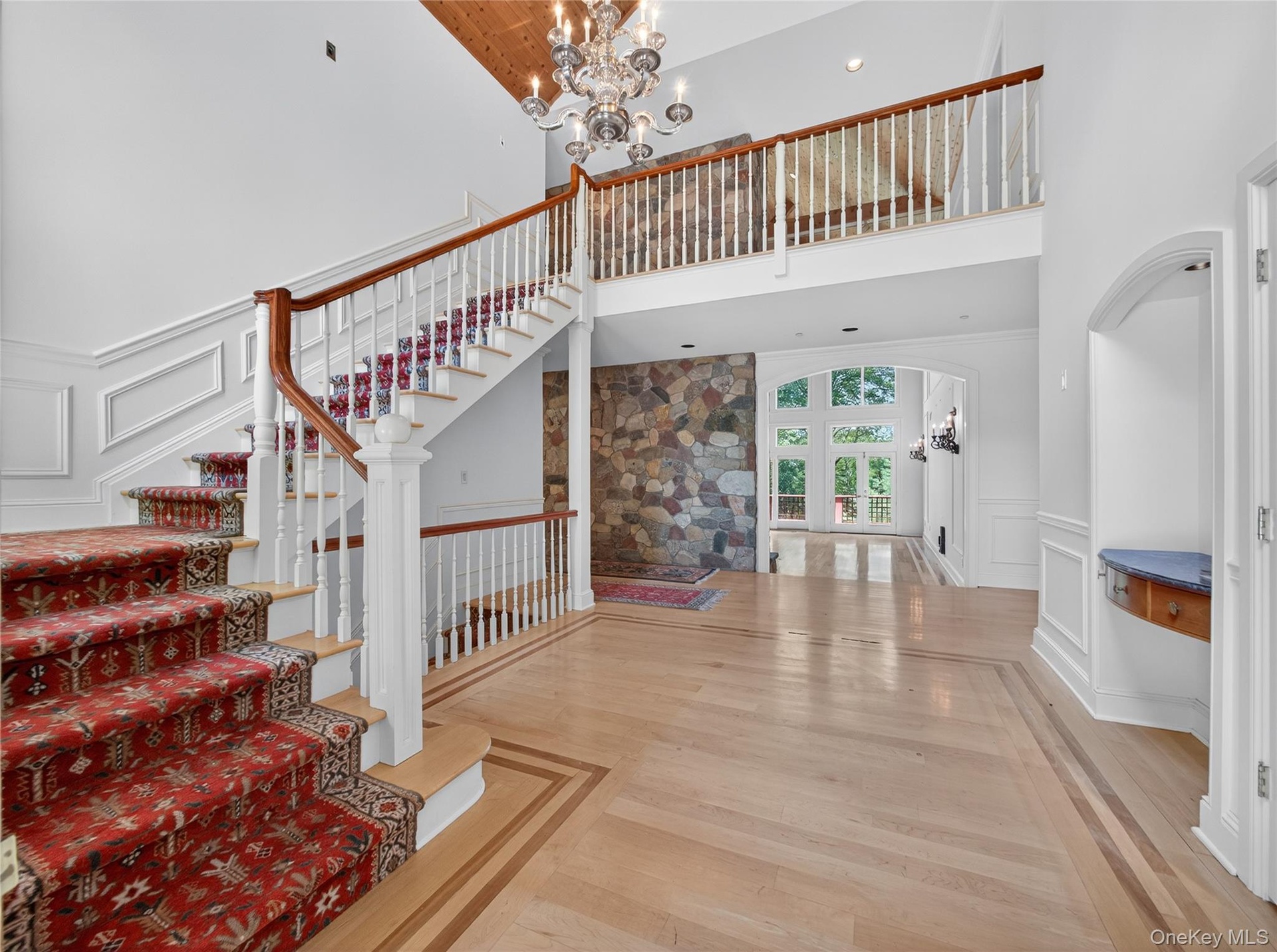 Stairway with a chandelier, a towering ceiling, a decorative wall, wood finished floors, and arched walkways