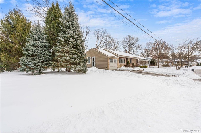 View of snow covered exterior featuring a garage and mature Evergreen trees.