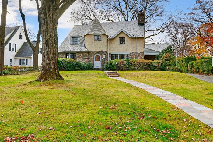 View of front of house featuring stone siding, a chimney, a front lawn, and a high end roof