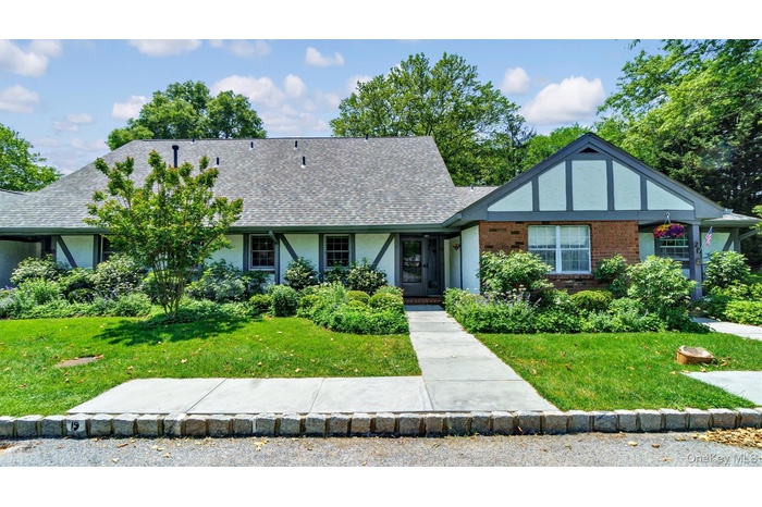 English style home with stucco siding, a front yard, roof with shingles, and brick siding