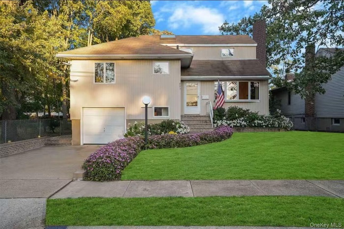 Tri-level home featuring a garage, a chimney, driveway, and roof with shingles