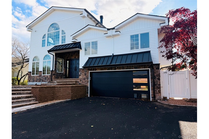 View of front of property with a standing seam roof, stone siding, a metal roof, and driveway