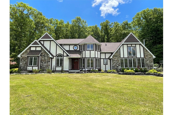 Tudor-style house with stone siding, stucco siding, a front yard, and roof with shingles